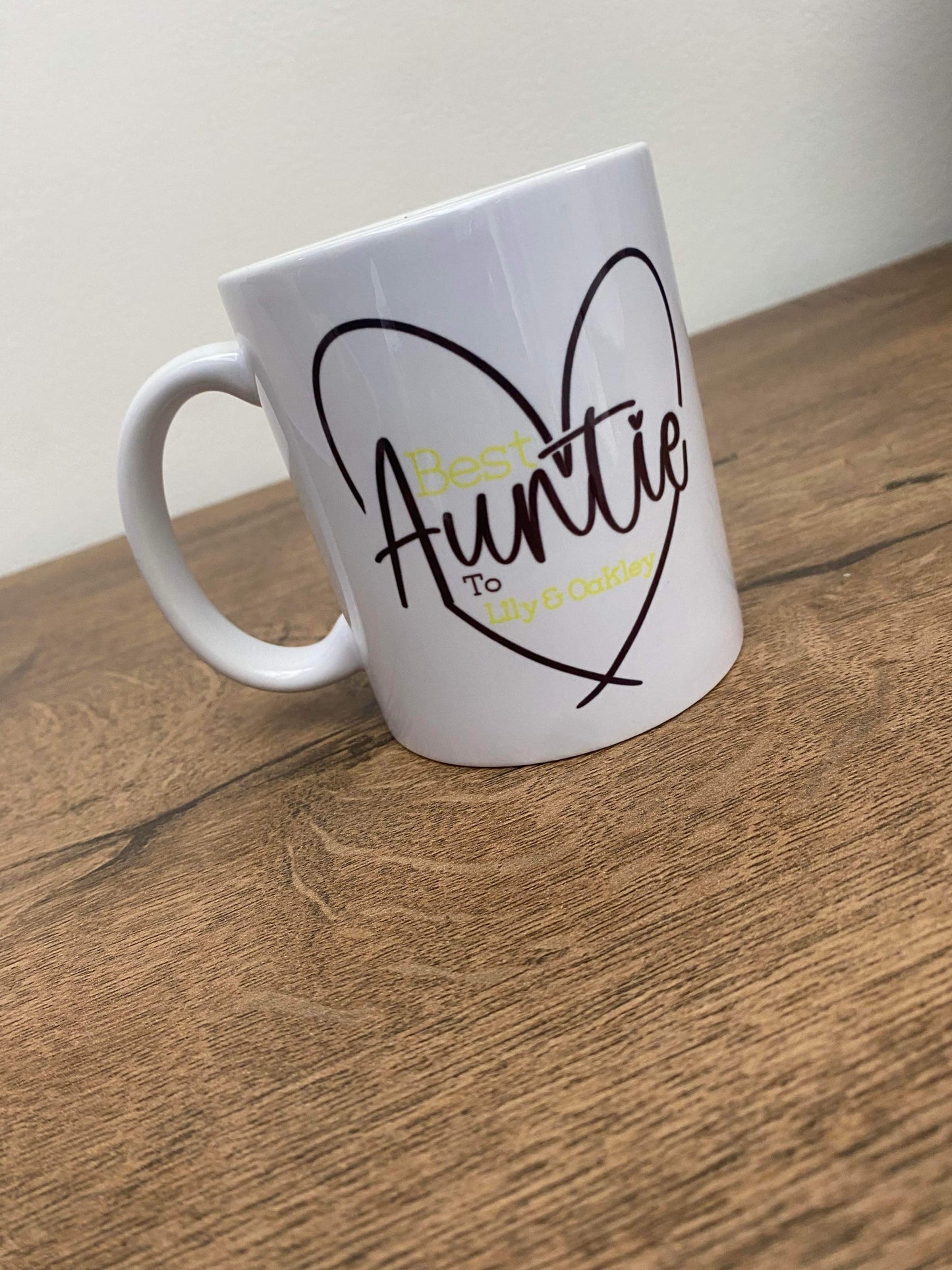A white ceramic mug with a heart-shaped cut-out on the top, personalized with the text 'Best Auntie' in yellow.