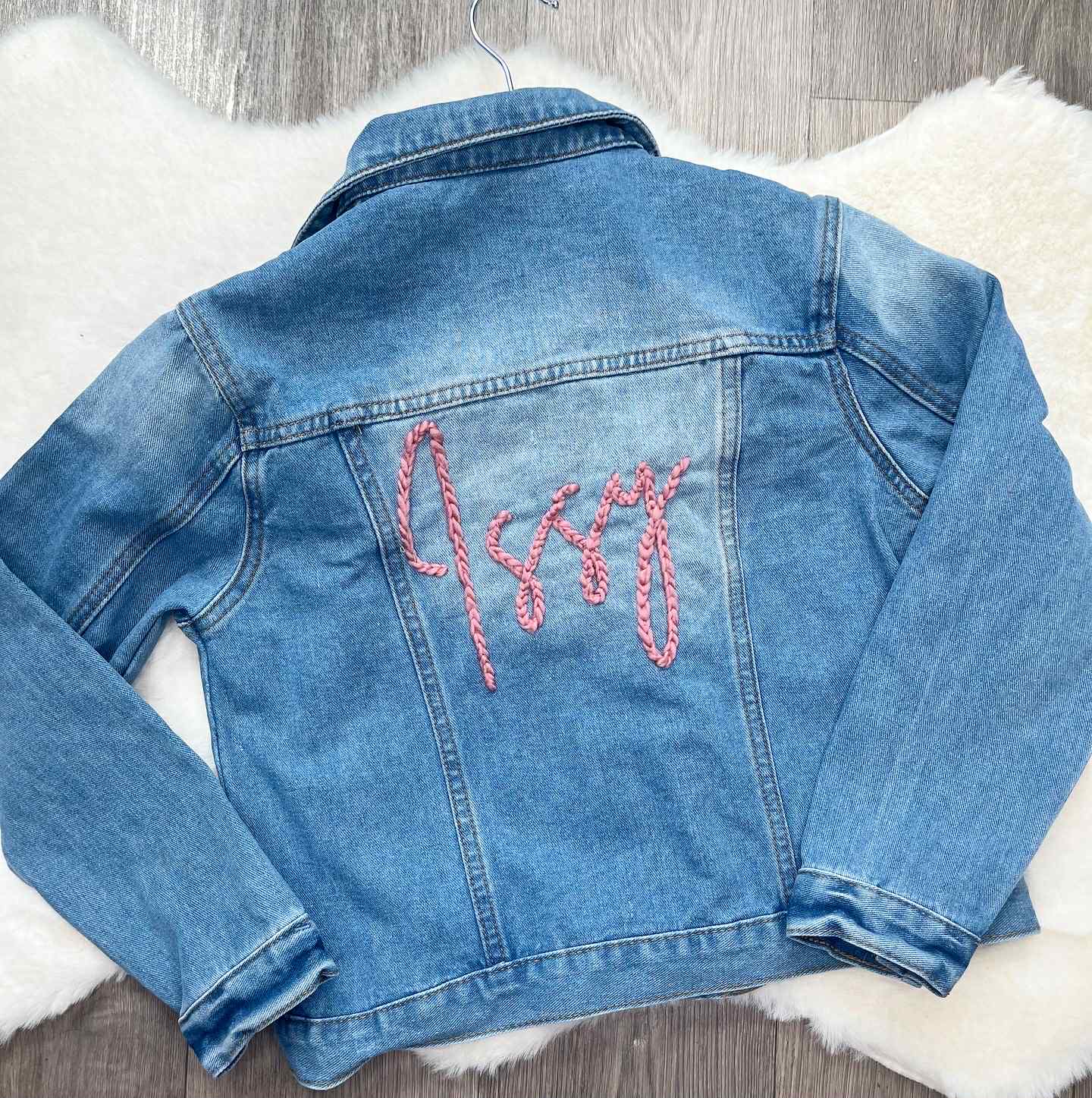 Blue denim jacket with pink embroidered text on a white surface