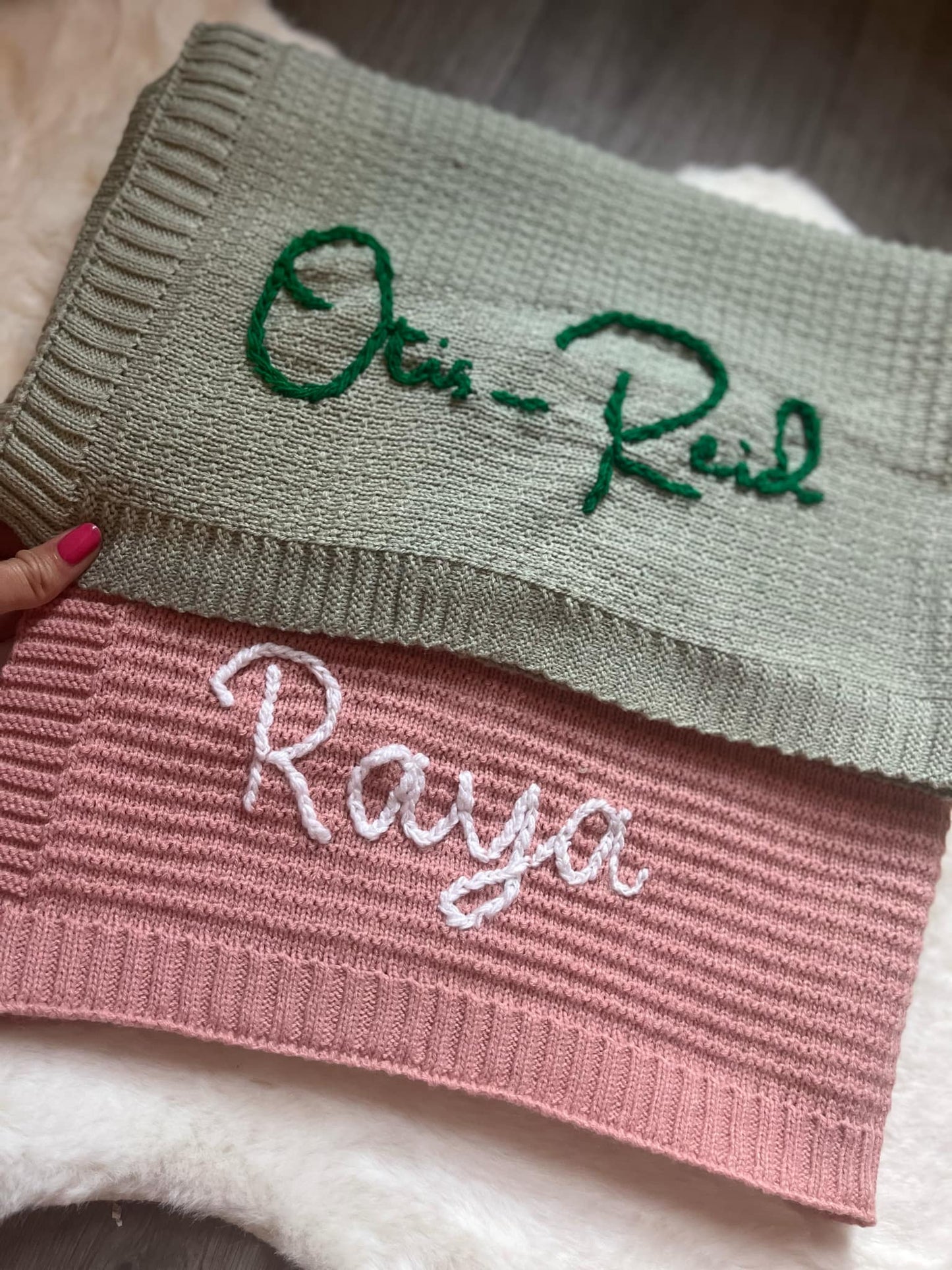 Two knitted items with embroidered names, one green and one pink, on a textured surface.
