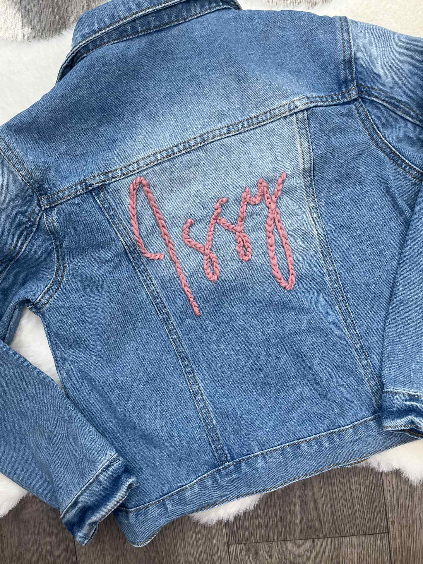 Blue denim jacket with pink embroidery on a wooden surface