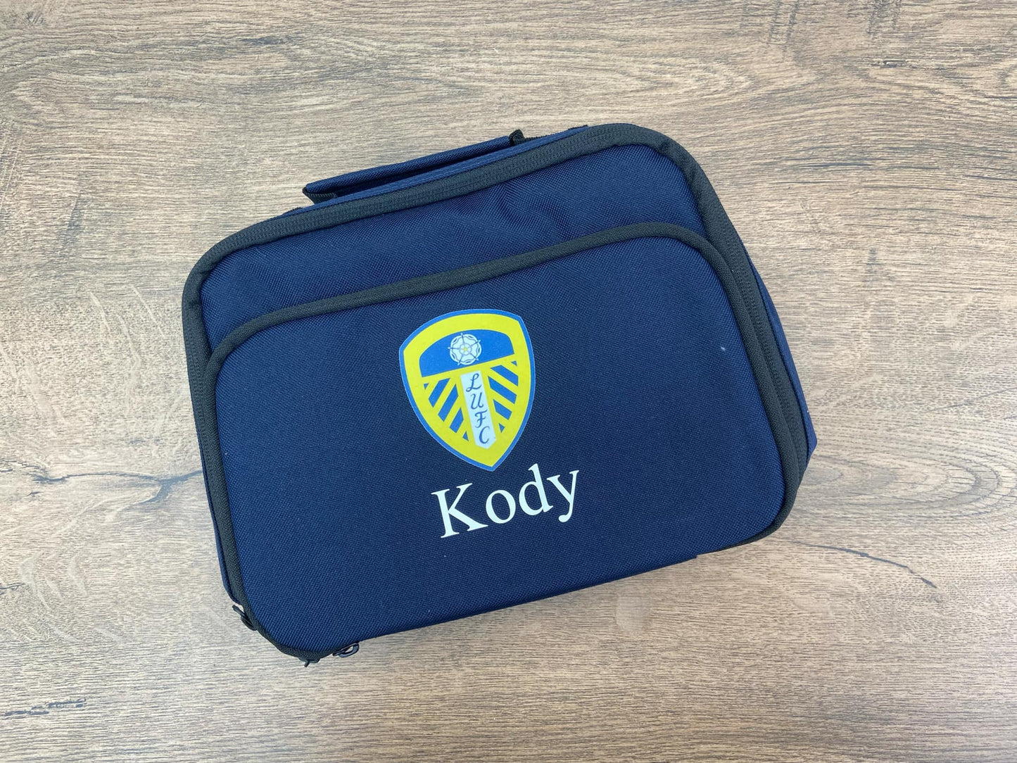 Navy blue Lunch bag with a logo and 'Kody' text on a wooden surface
