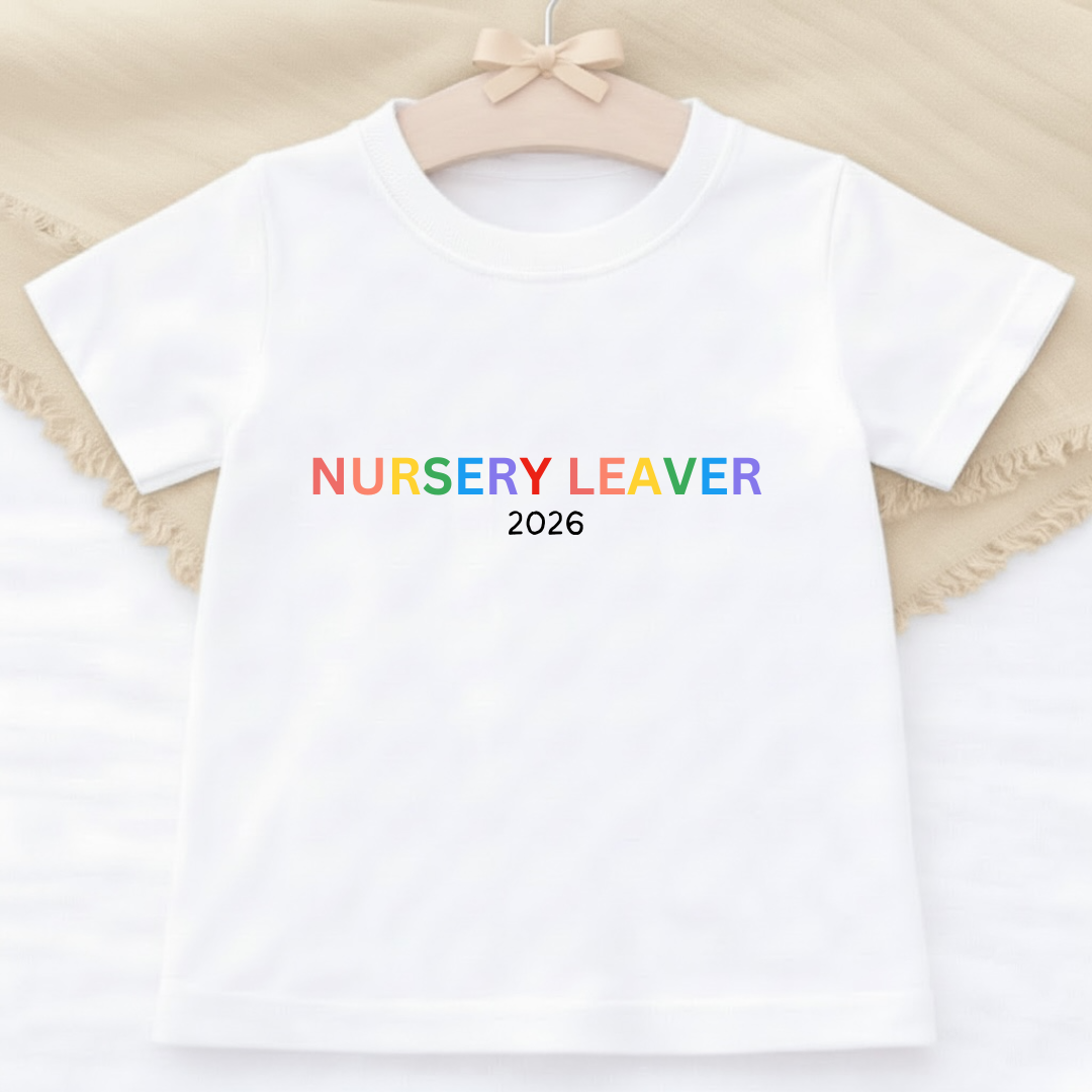 White t-shirt with 'NURSERY LEAVER 2026' text in rainbow colors on a beige background