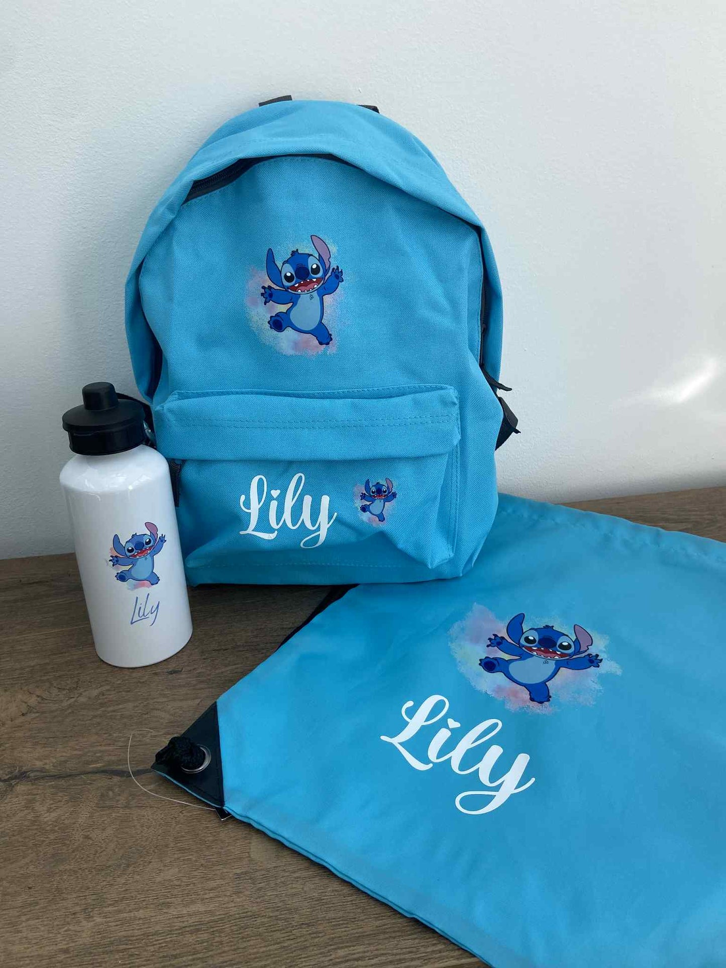Blue backpack, water bottle, and pouch with 'Lily' and cartoon character on a wooden surface.