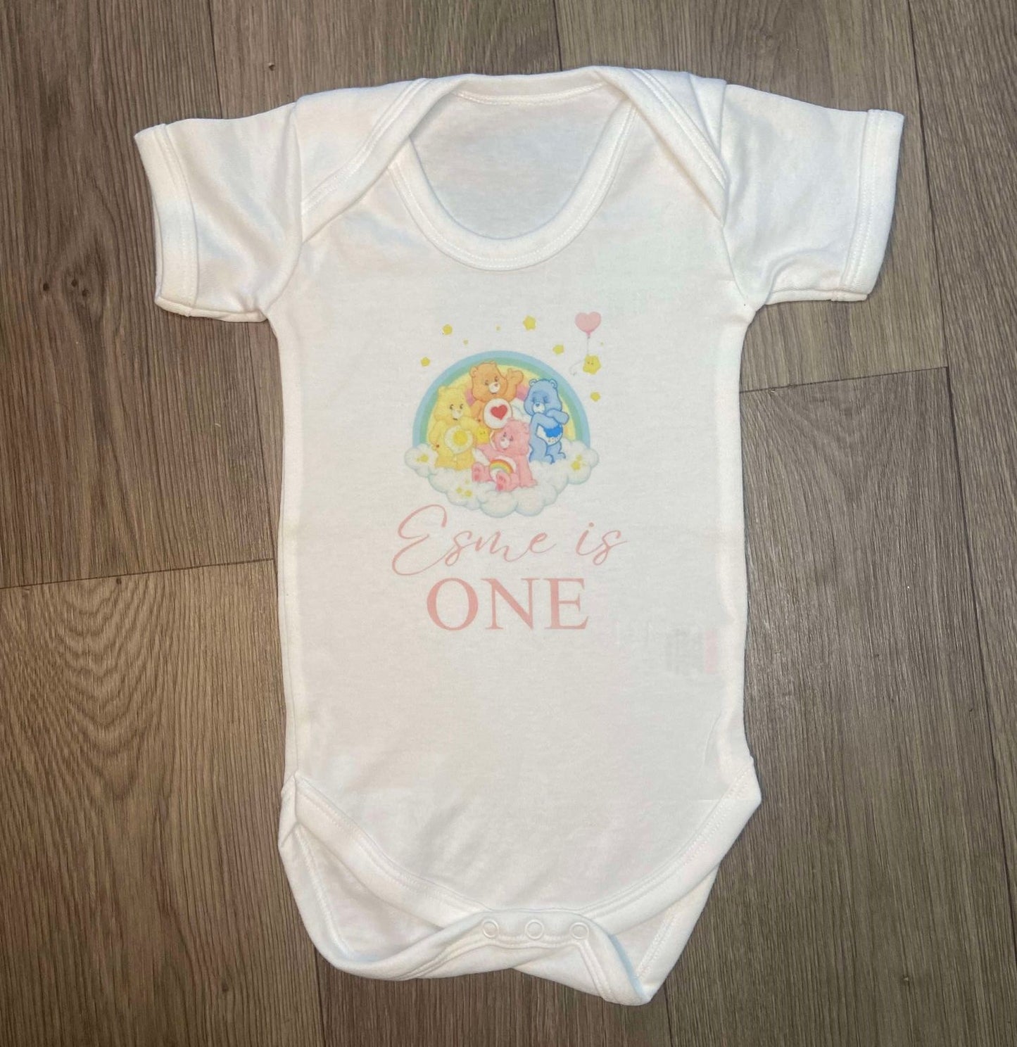 White Cotton Baby Vest Personalised with image of care bears on a rainbows/clouds with ' Esme is ONE'