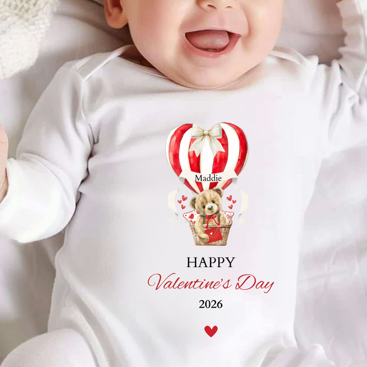 Baby wearing a Valentine's Day-themed onesie with a teddy bear and hot air balloon design.