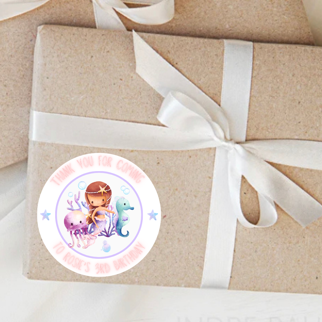 Gift wrapped in brown paper with a white ribbon and a colorful sticker featuring a mermaid and seahorse on a white background.