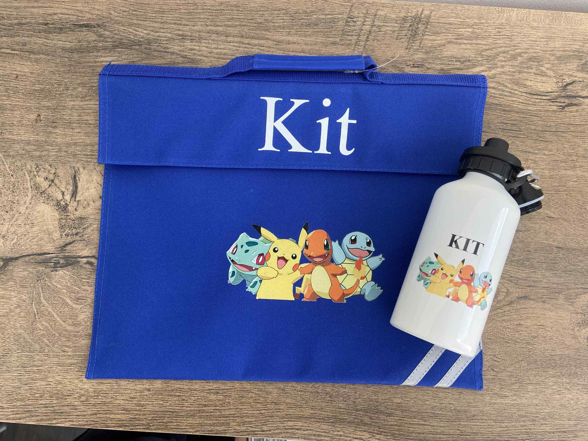 Blue Book bag with cartoon characters and 'Kit' text, next to a white water bottle with similar design on a wooden surface.