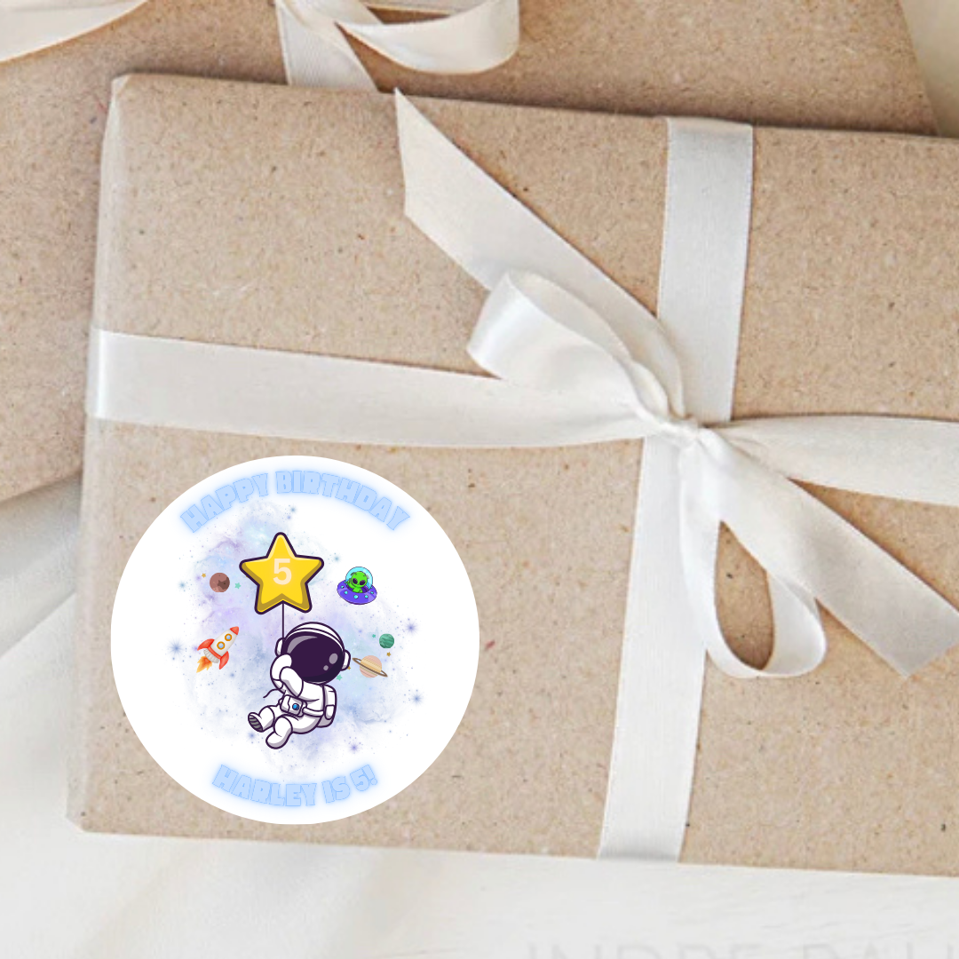 Gift box wrapped in brown paper with a white ribbon and a 'Happy Birthday' sticker featuring an astronaut and star.
