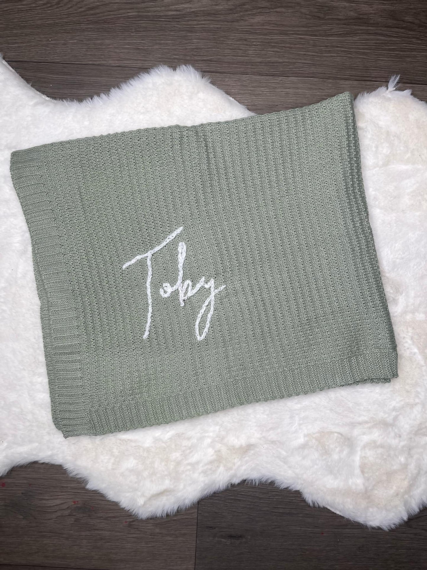 Green knitted blanket with 'Toby' embroidery on a textured surface