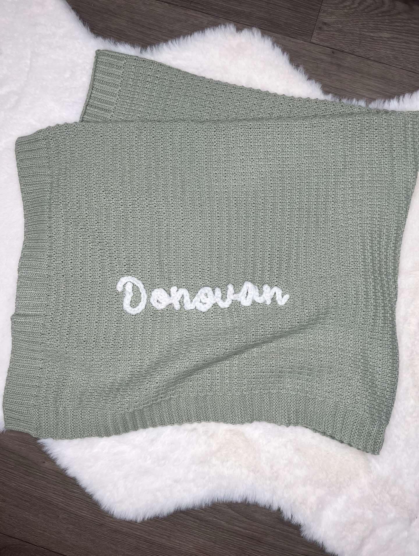 Green knitted blanket with 'Donovan' embroidery on a textured surface