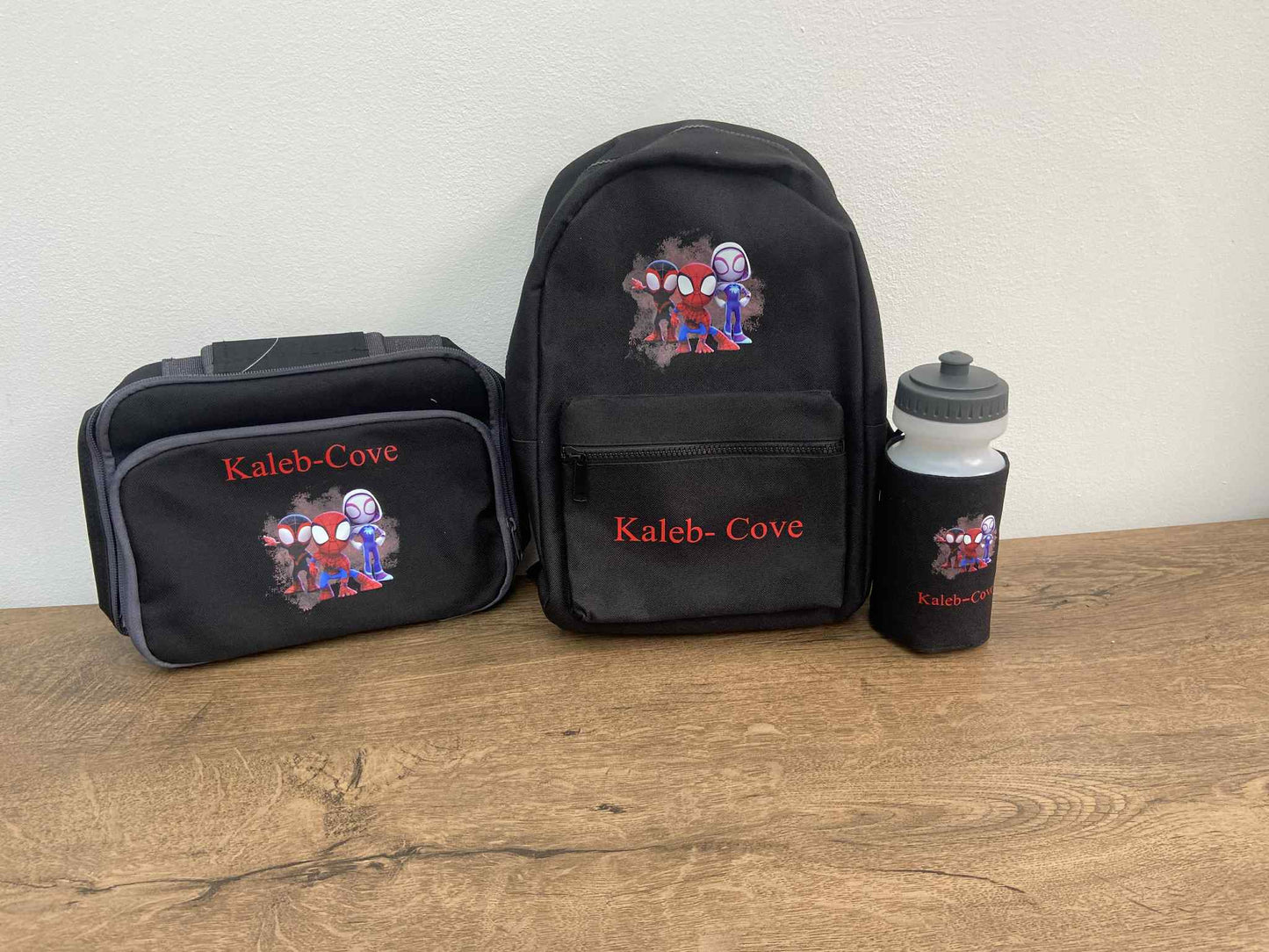 Black backpack, lunch bag, and water bottle with 'Kaleb Cove' branding on a wooden surface.