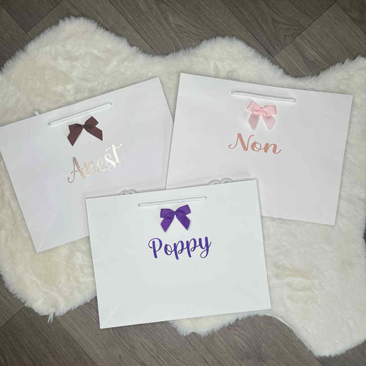 Three white gift bags with personalised names and bows on a fluffy white rug.