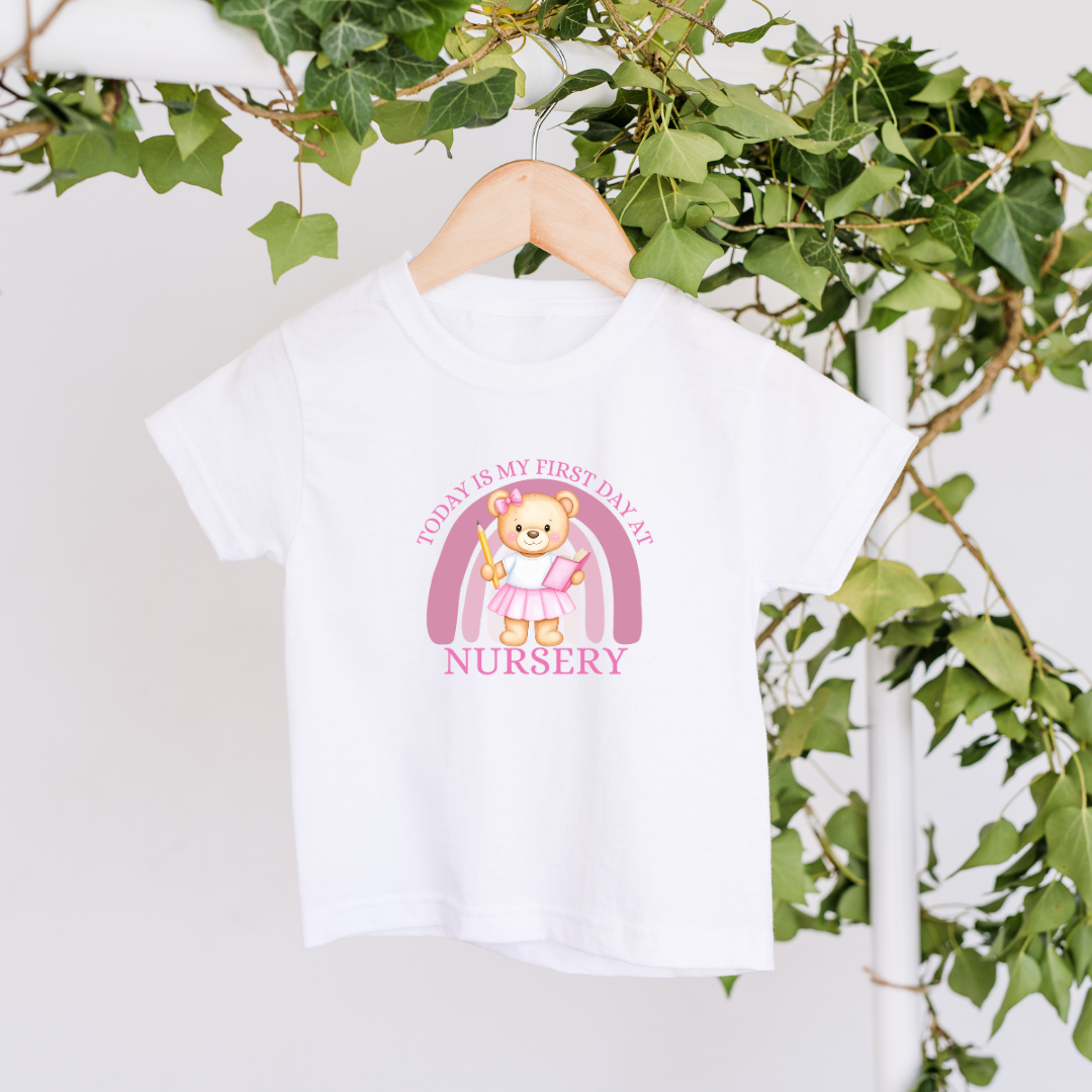 White t-shirt with a teddy bear graphic and text on a hanger against a green leafy background