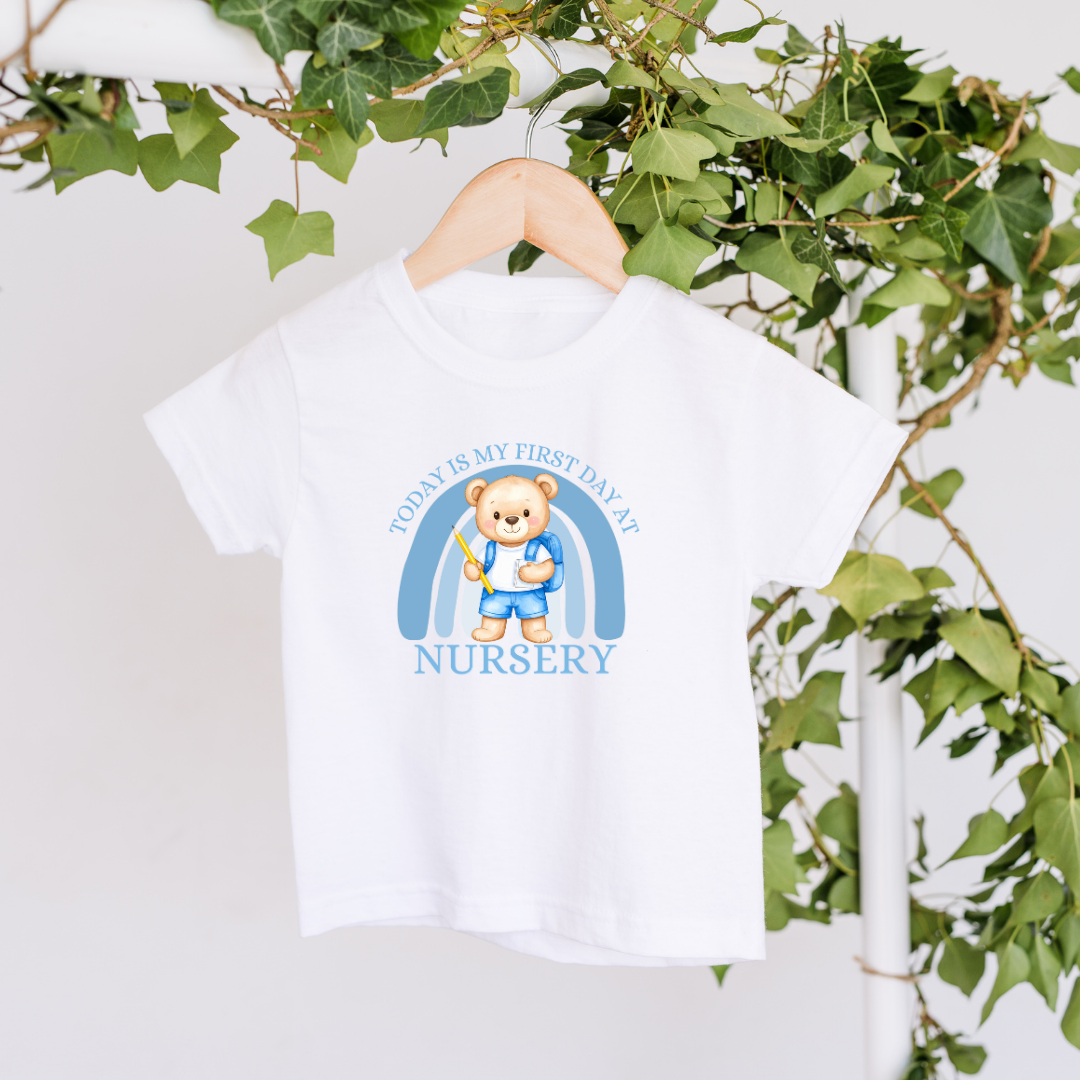 White t-shirt with a teddy bear design and text on a hanger with green leaves in the background