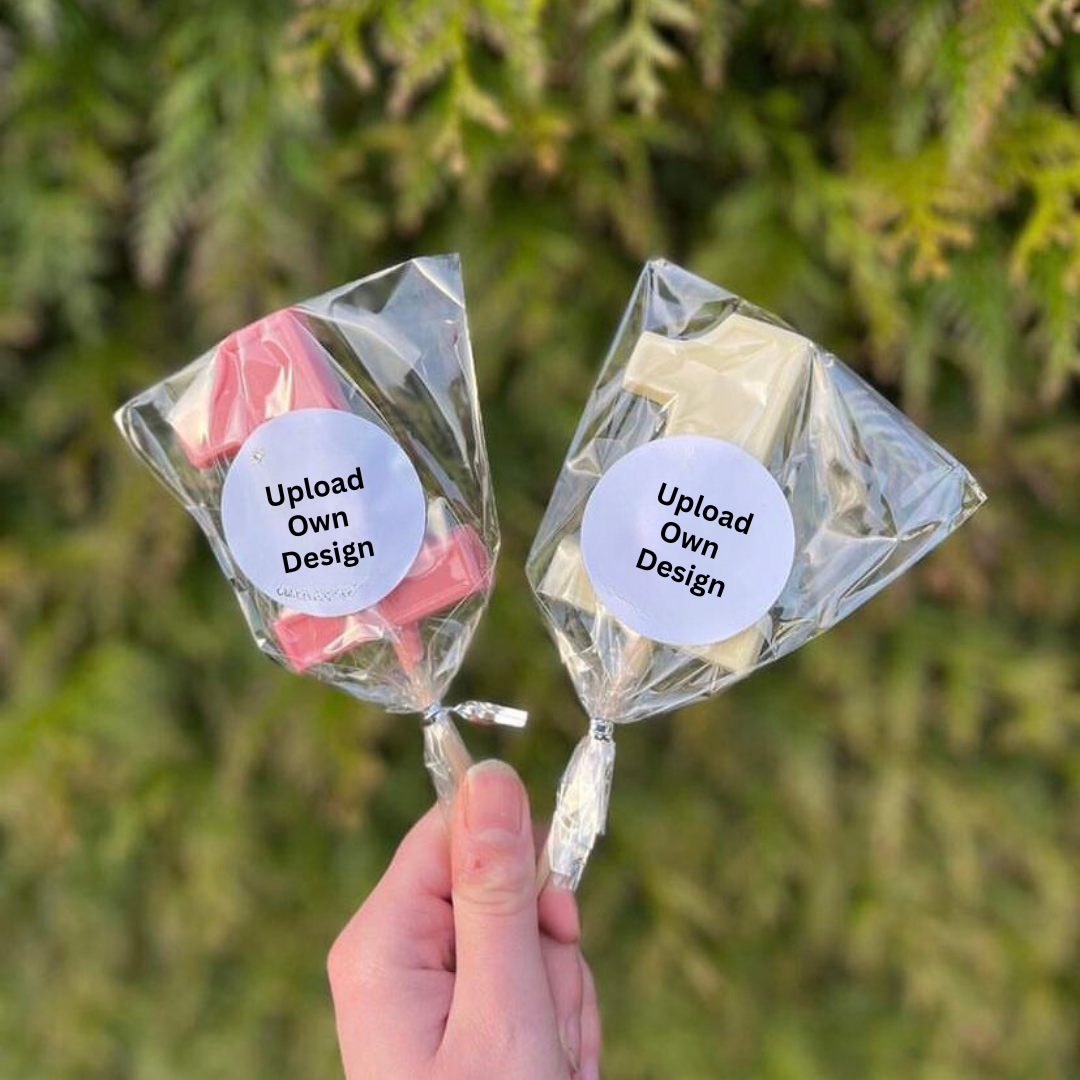 Two personalized stickers with upload own design labels, one pink and one white, held in a person's hand against a blurred greenery background.