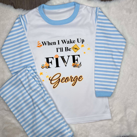 Blue striped pyjamas with text saying when I wake up I’ll be and images of diggers and construction equipment 