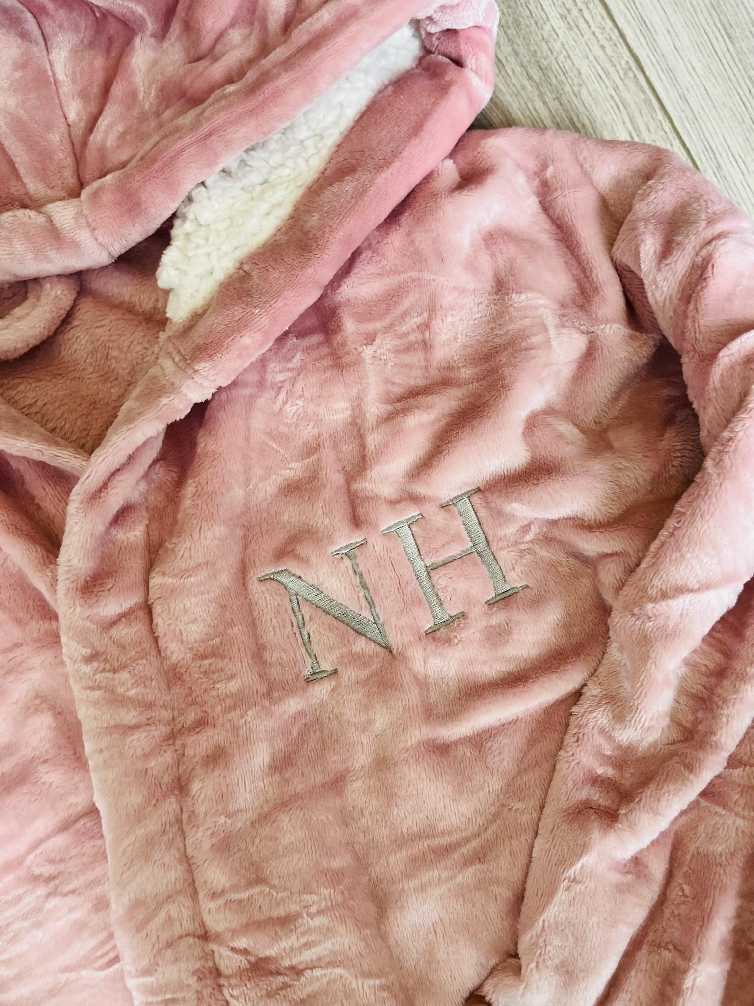 Pink plush blanket with 'NH' initials on a wooden surface