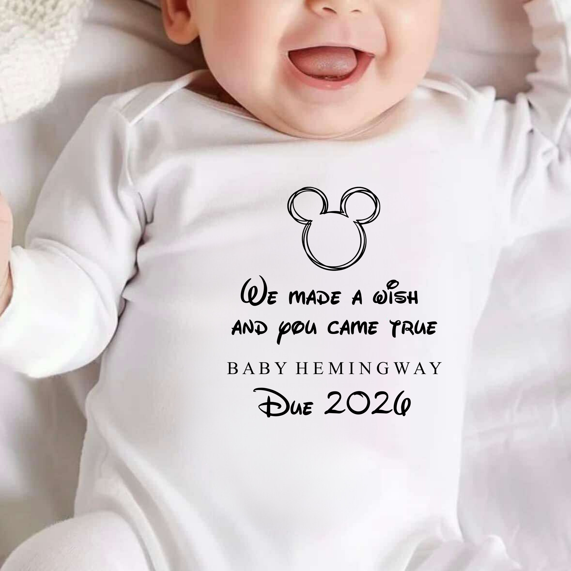 Baby wearing a white onesie with text and a Mickey Mouse icon.