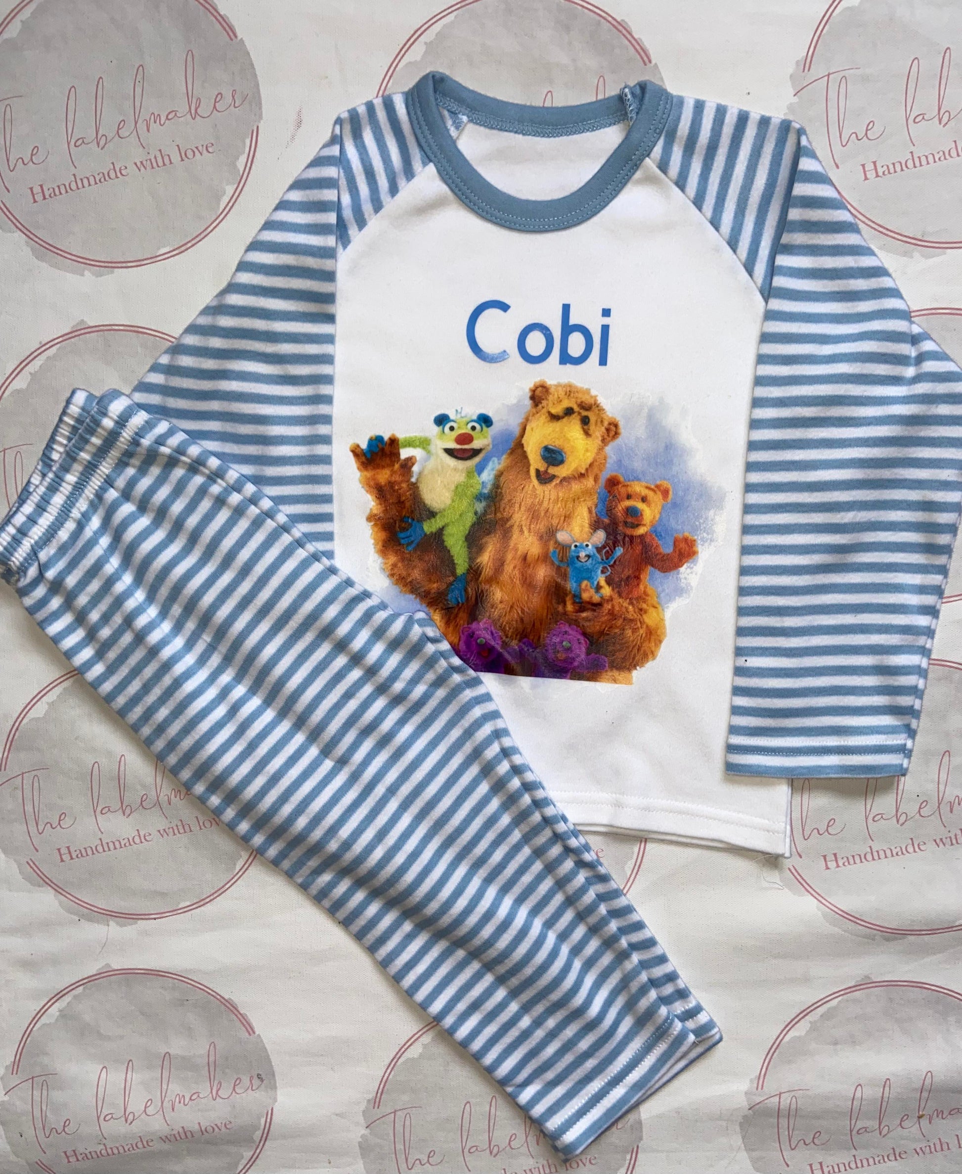 A set of children's pyjamas with blue and white stripes featuring colorful bear characters and the name 'Cobi' on the shirt.
