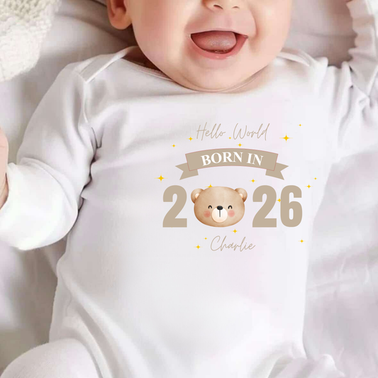 Baby wearing a white onesie with 'Born in 2026' and a bear illustration.