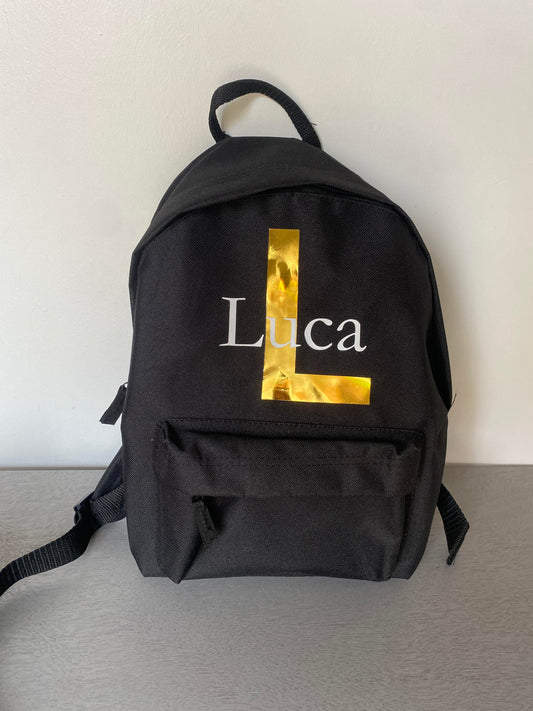 Black 7 litre backpack with gold and white name and inital.