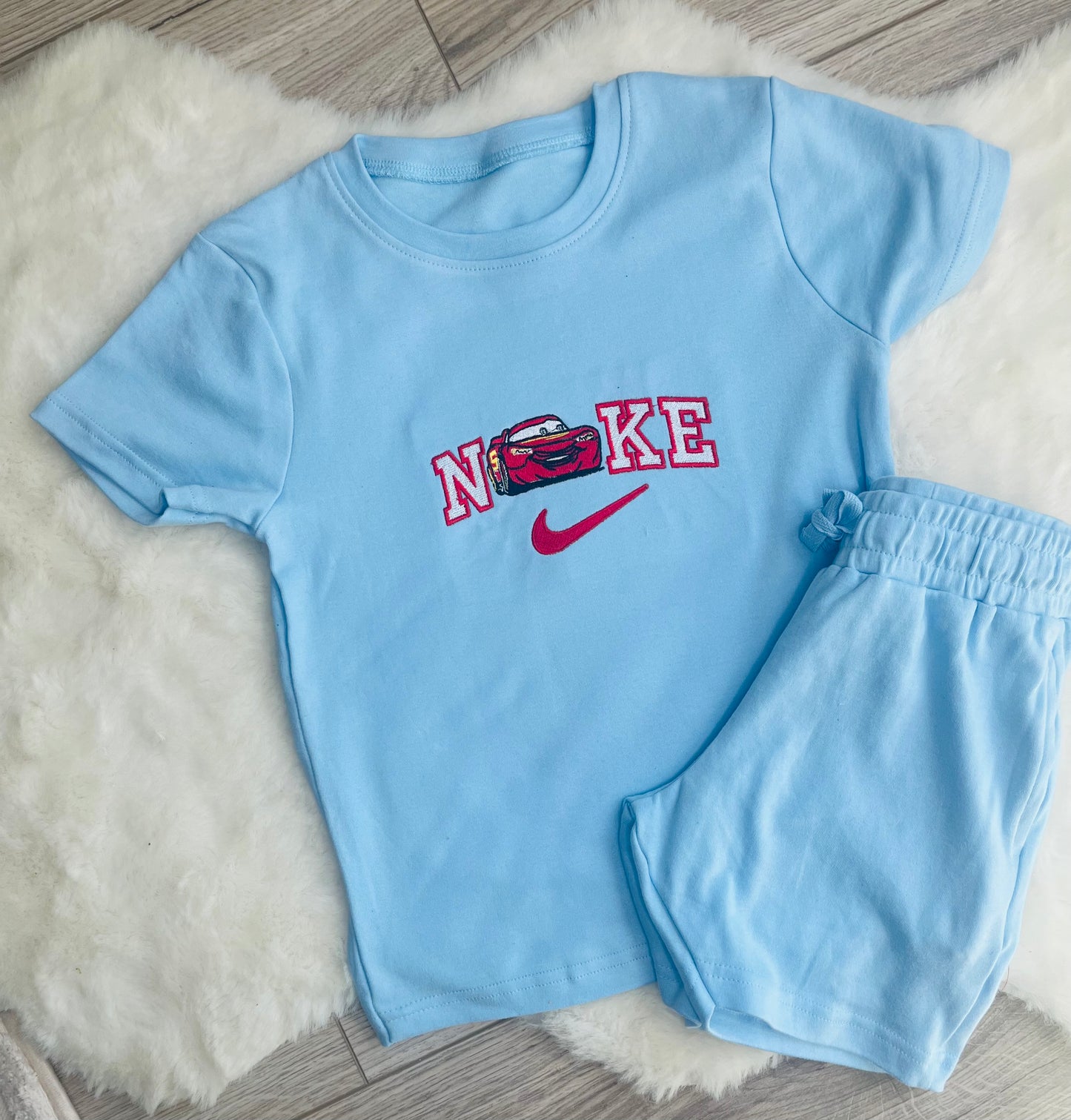 Blue personalised children’s summer short set with embroidered character inspired design and matching shorts on white rug