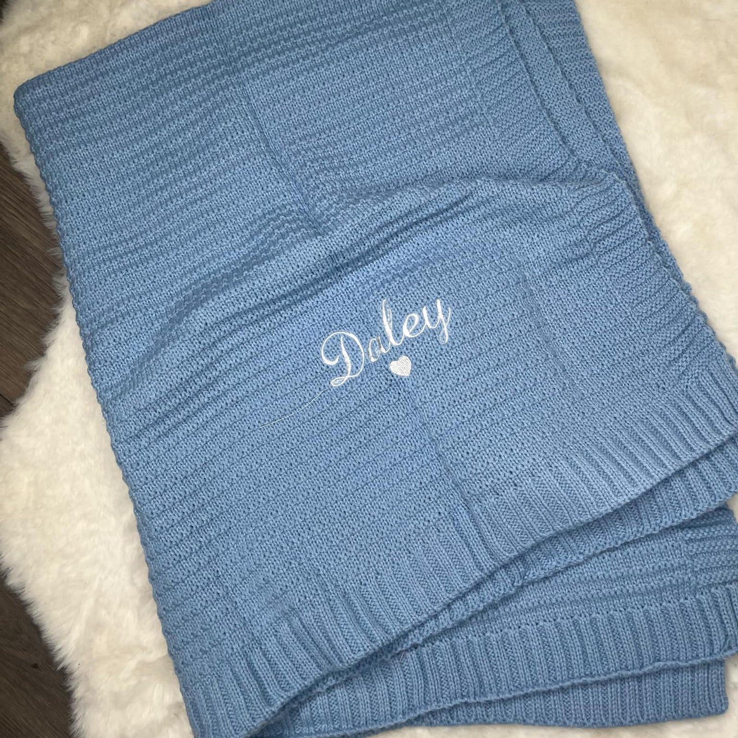 Blue knitted blanket with 'Daley' embroidery on a white surface