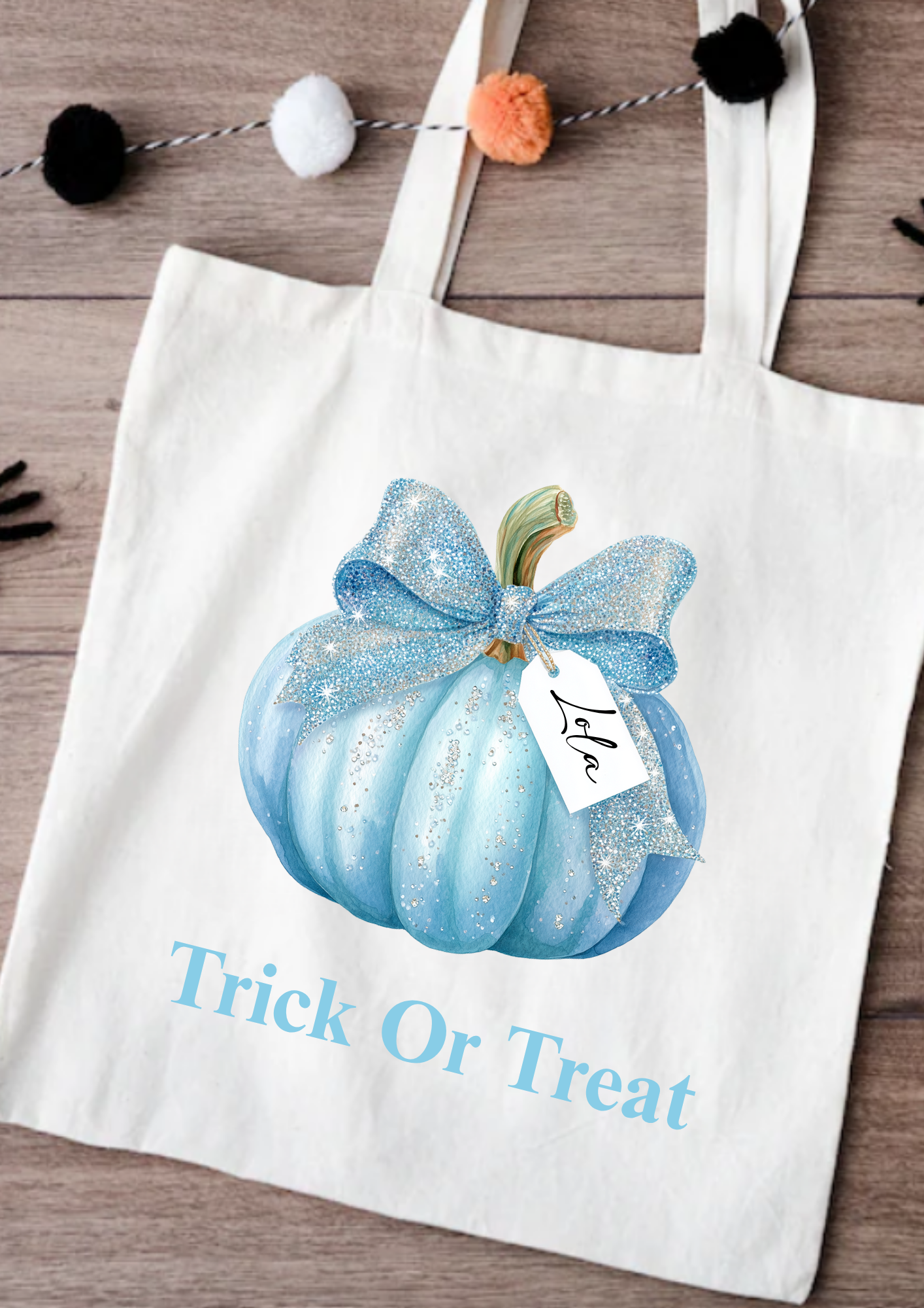 White tote bag with blue pumpkin and bow design, featuring 'Trick or Treat' text on a wooden surface.
