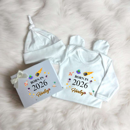 Baby outfit set with 'Born in 2026' shirt, hat, and box on a soft surface