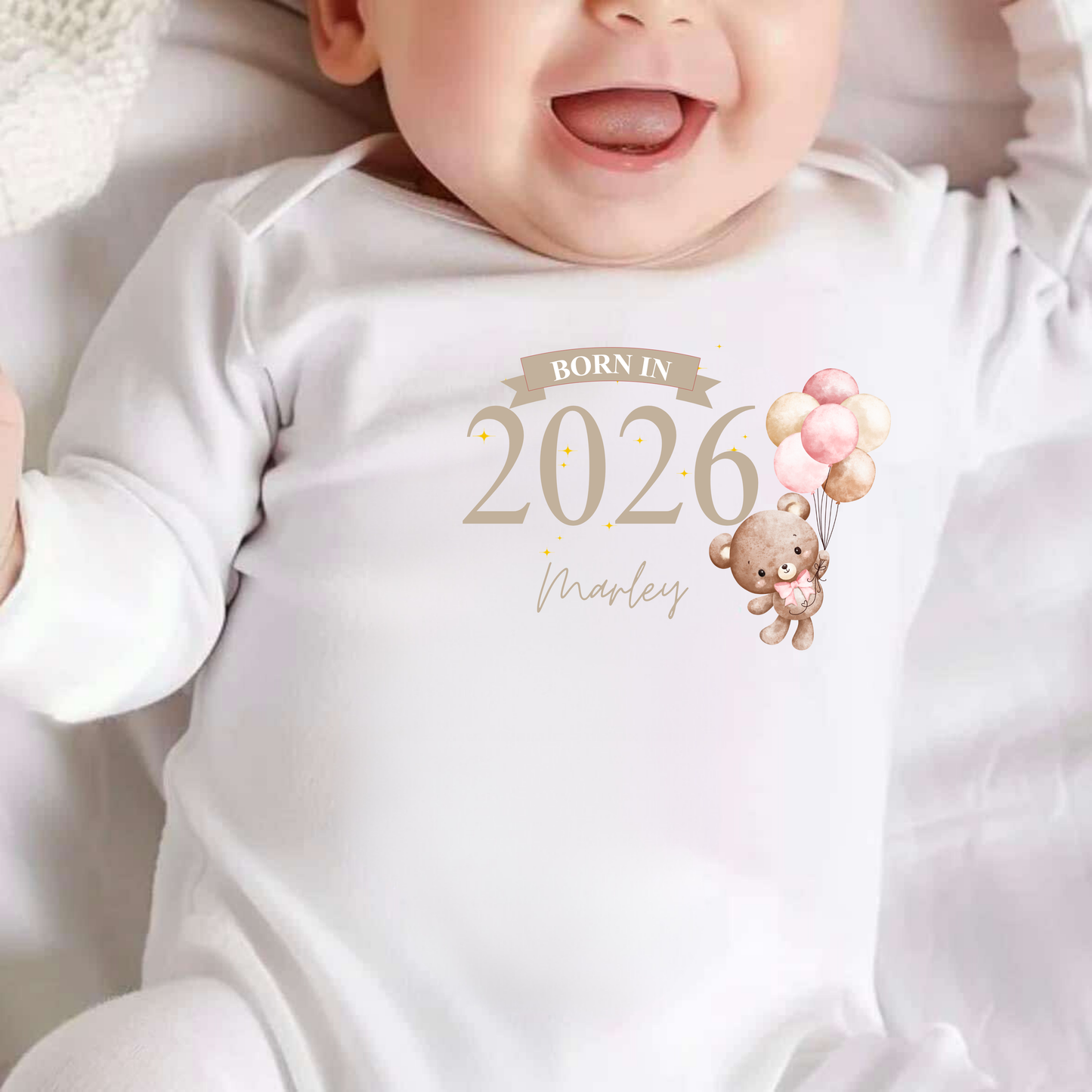 Baby wearing a white onesie with 'Born in 2026' text and teddy bear design.