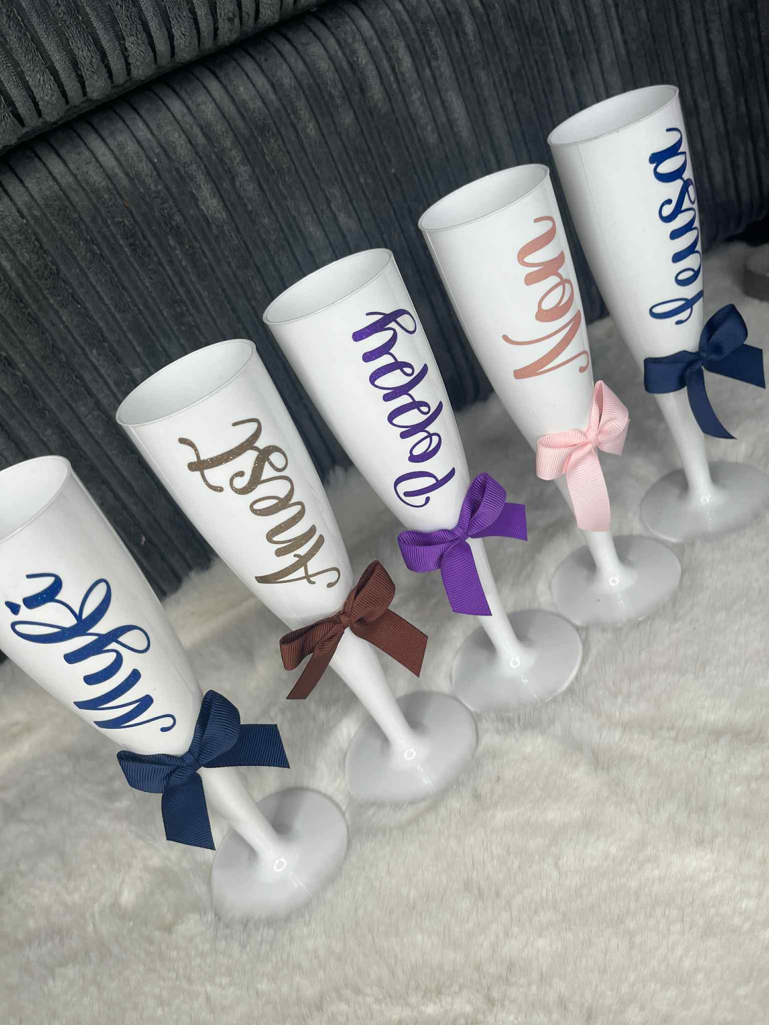 Set of personalised white champagne flutes with names and colourful bows .