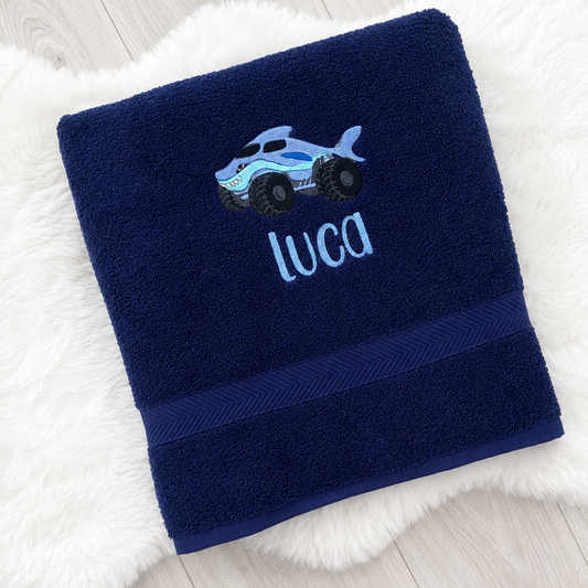Navy blue towel with a car design and 'Luca' text on a white fluffy surface.