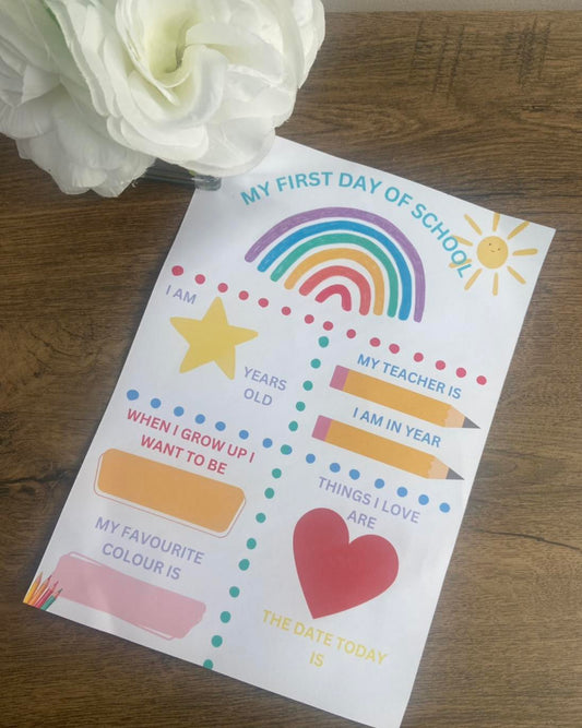 A colorful First Day of School print with spaces for writing and drawing, placed on a table with a white flower in the background.