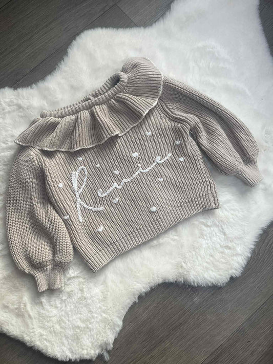 Knitted baby outfit with ruffled details on a fluffy white surface