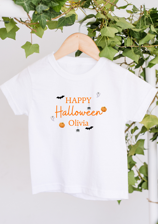 White t-shirt with 'Happy Halloween Olivia' text on a hanger with greenery in the background