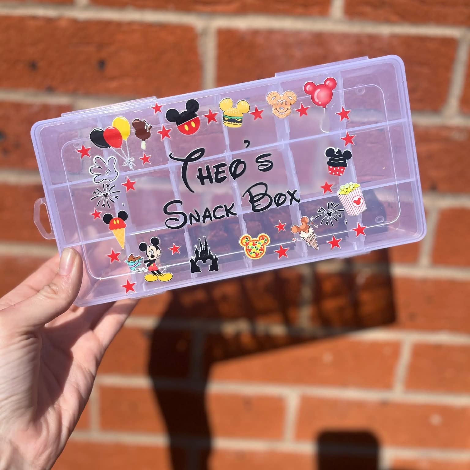 Clear snack box with cartoon character designs held by a hand against a brick wall.