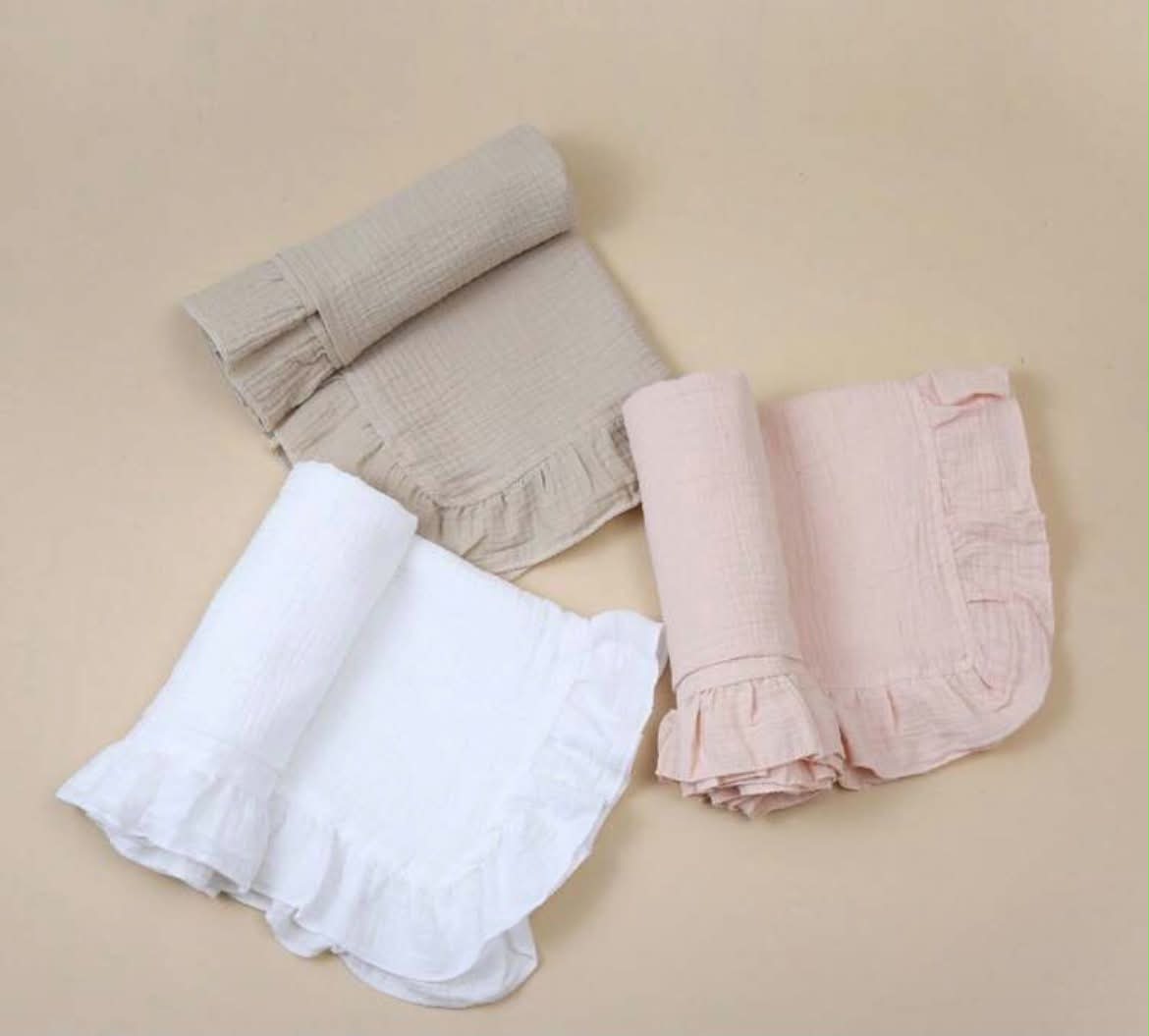 Three folded gauze muslin baby swaddle blankets in beige, white, and light pink, arranged on a solid beige background.