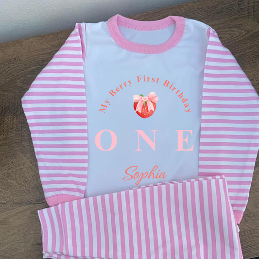 Pink and white striped children's outfit with 'My Berry First Birthday ONE Sophia' text on a wooden surface.
