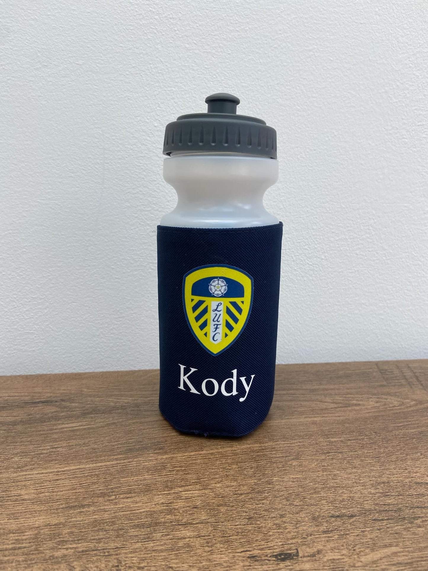 Water bottle with navy blue sleeve and yellow logo on a wooden surface