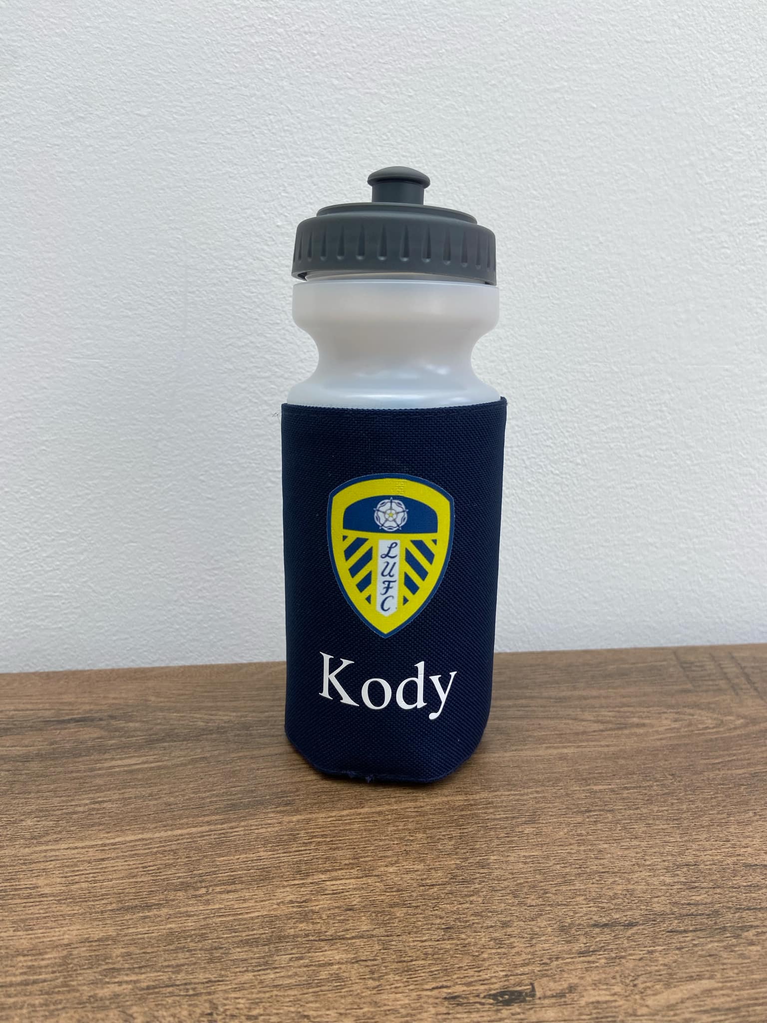 Water bottle with navy blue sleeve and yellow logo on a wooden surface