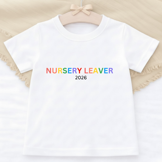 White t-shirt with 'NURSERY LEAVER 2026' text in rainbow colors on a beige background
