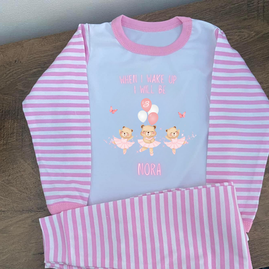 Pink and white striped pajama set with teddy bear design and text on a wooden surface