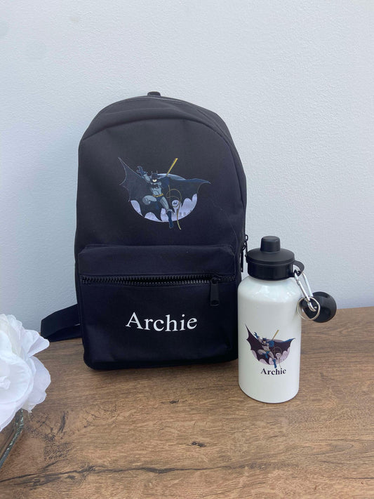 A black personalised backpack for children with a Bat Man design, accompanied by a white water bottle with a name 'Archie' printed on it.