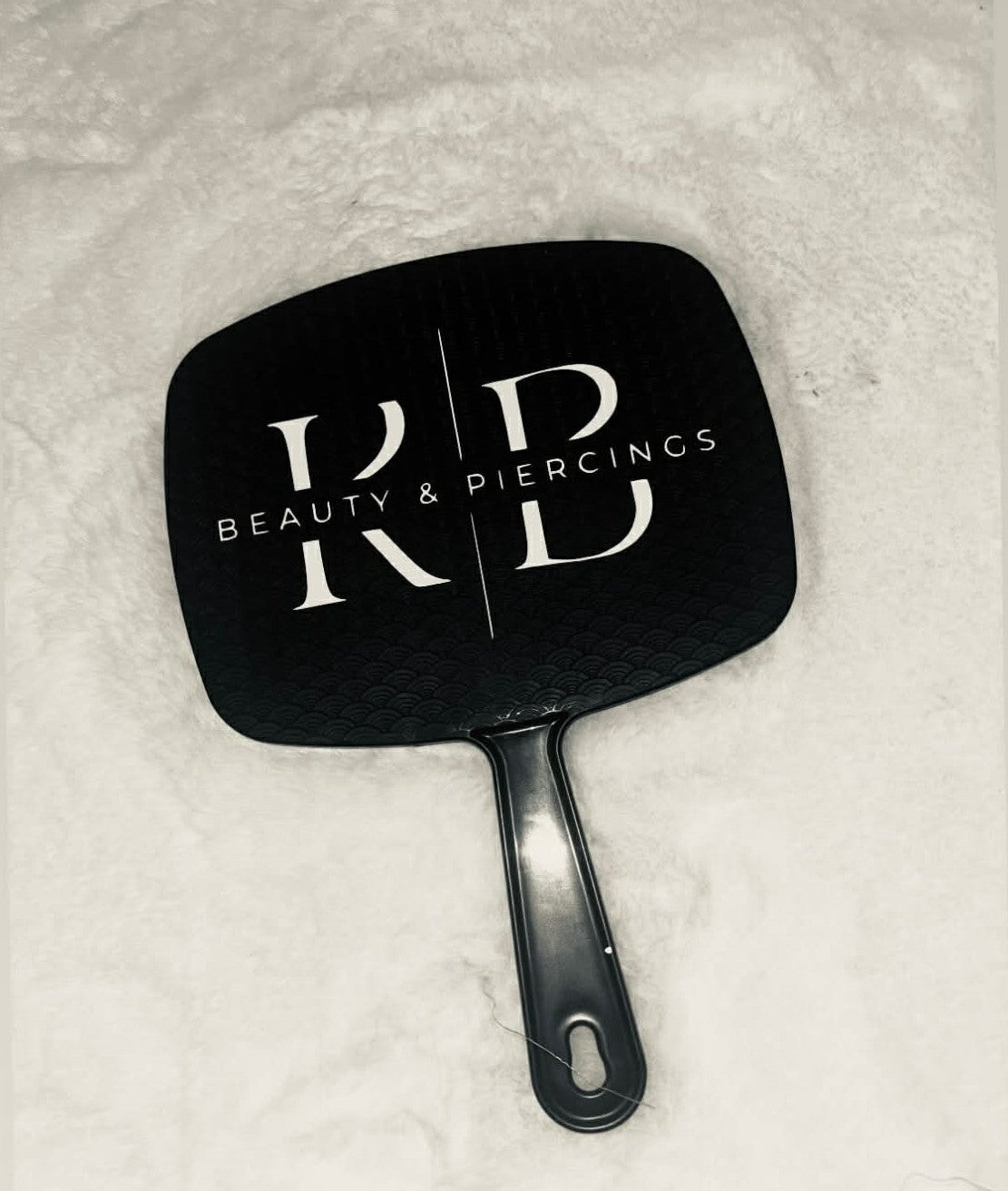 Black hand mirror with 'RD Beauty & Piercings' logo on a textured white background