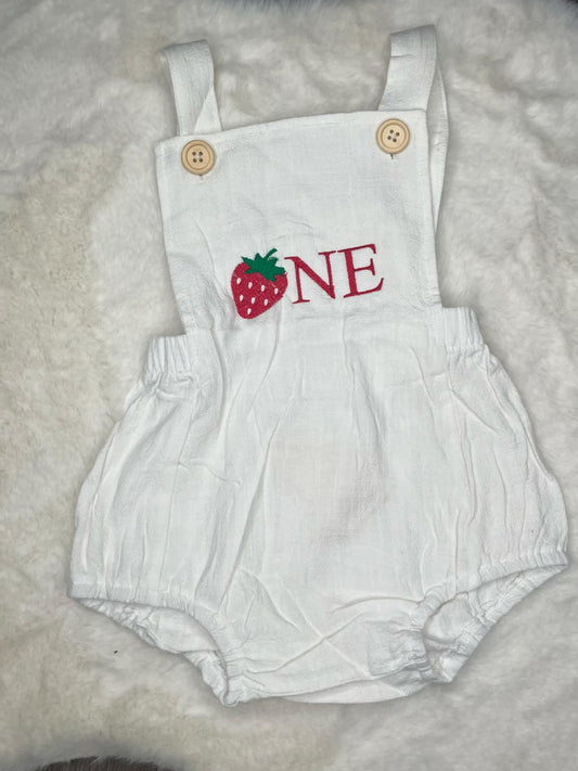 White romper with strawberry and 'ONE' text on a fluffy white surface