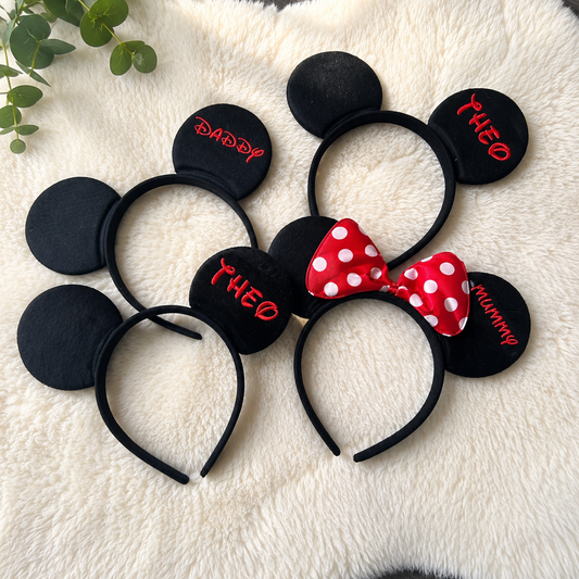 Black mouse ears headbands with personalised text on a fluffy white surface.