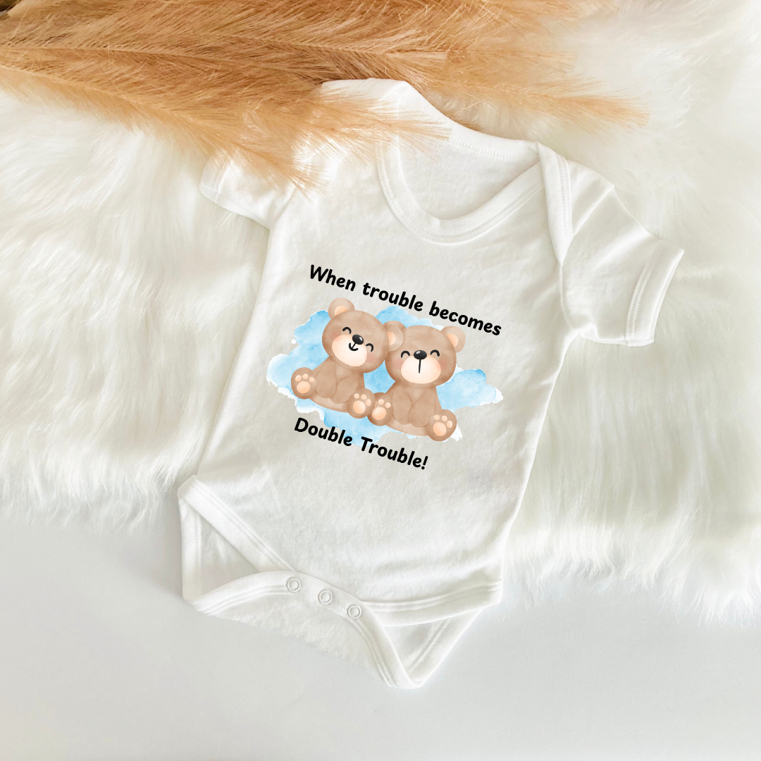 White baby onesie with teddy bear design and text on a fluffy white surface.