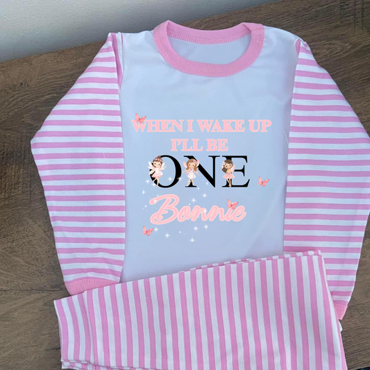Pink and white striped children's pyjamas set with personalised text on a wooden surface