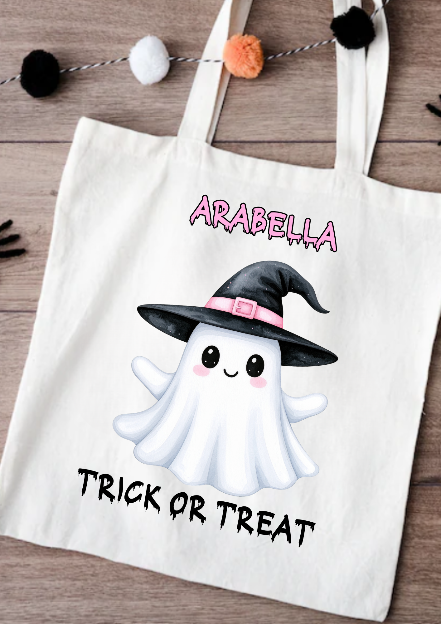 Tote bag with a ghost wearing a witch hat and 'Trick or Treat' text on a wooden surface.