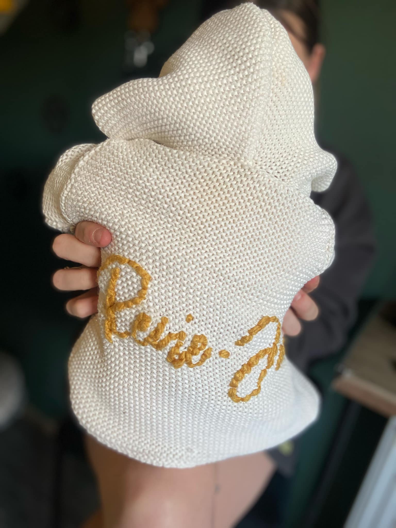 White knitted jacket  with gold text held by a person against a blurred background